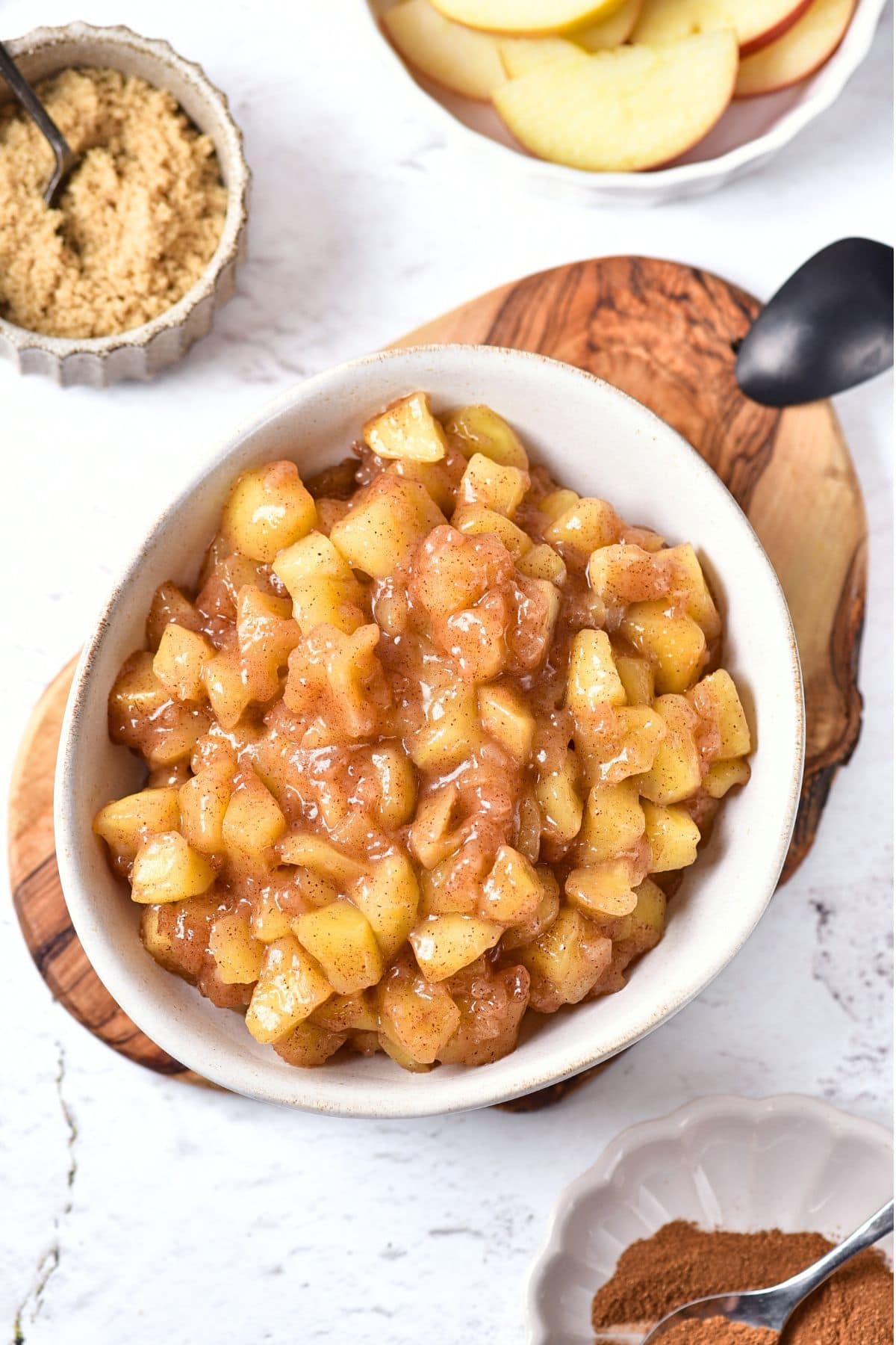 Top down view of a bowl of homemade apple pie filling on wooden board.