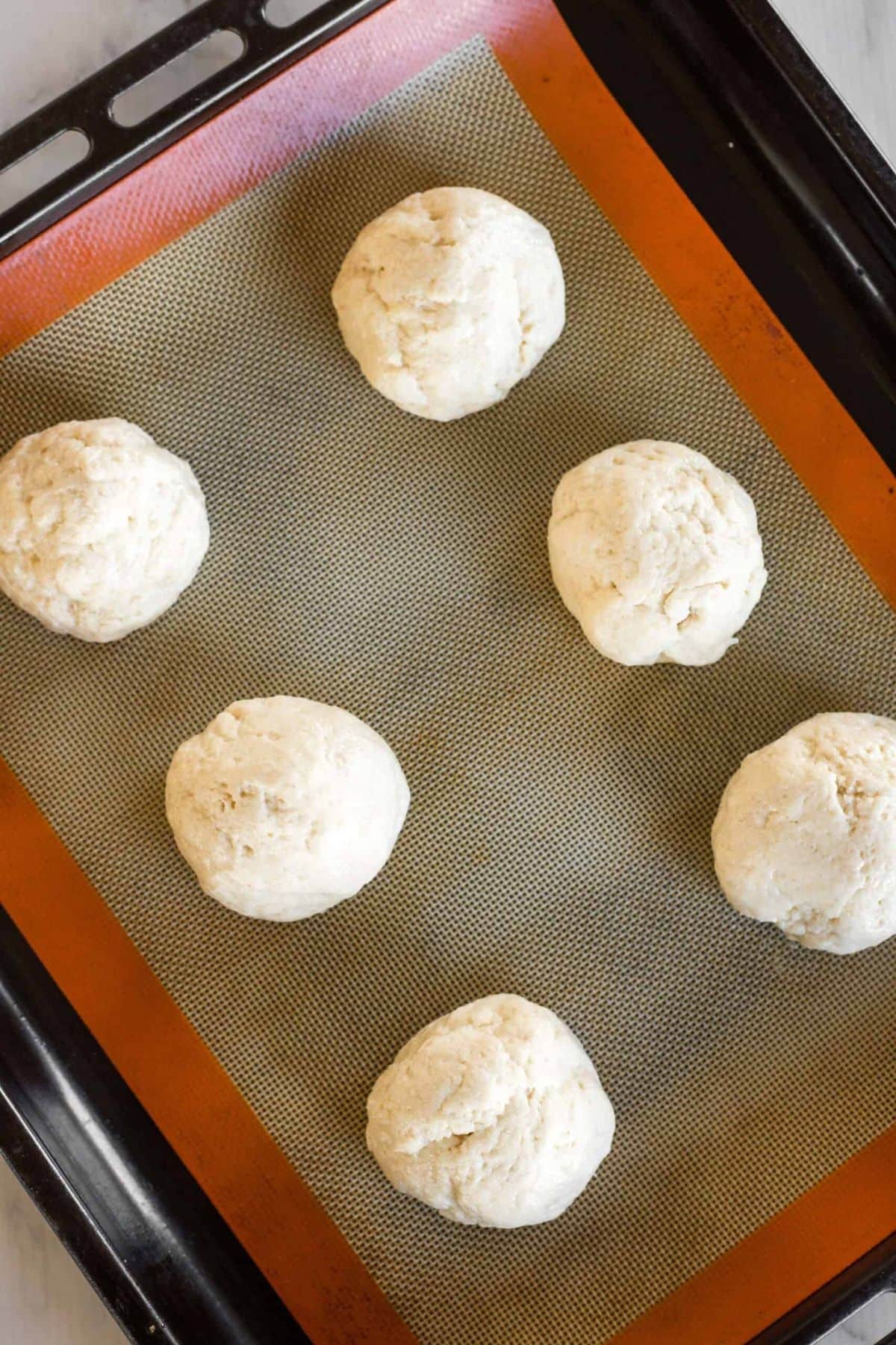 Balls of dough on silpat lined baking sheet.