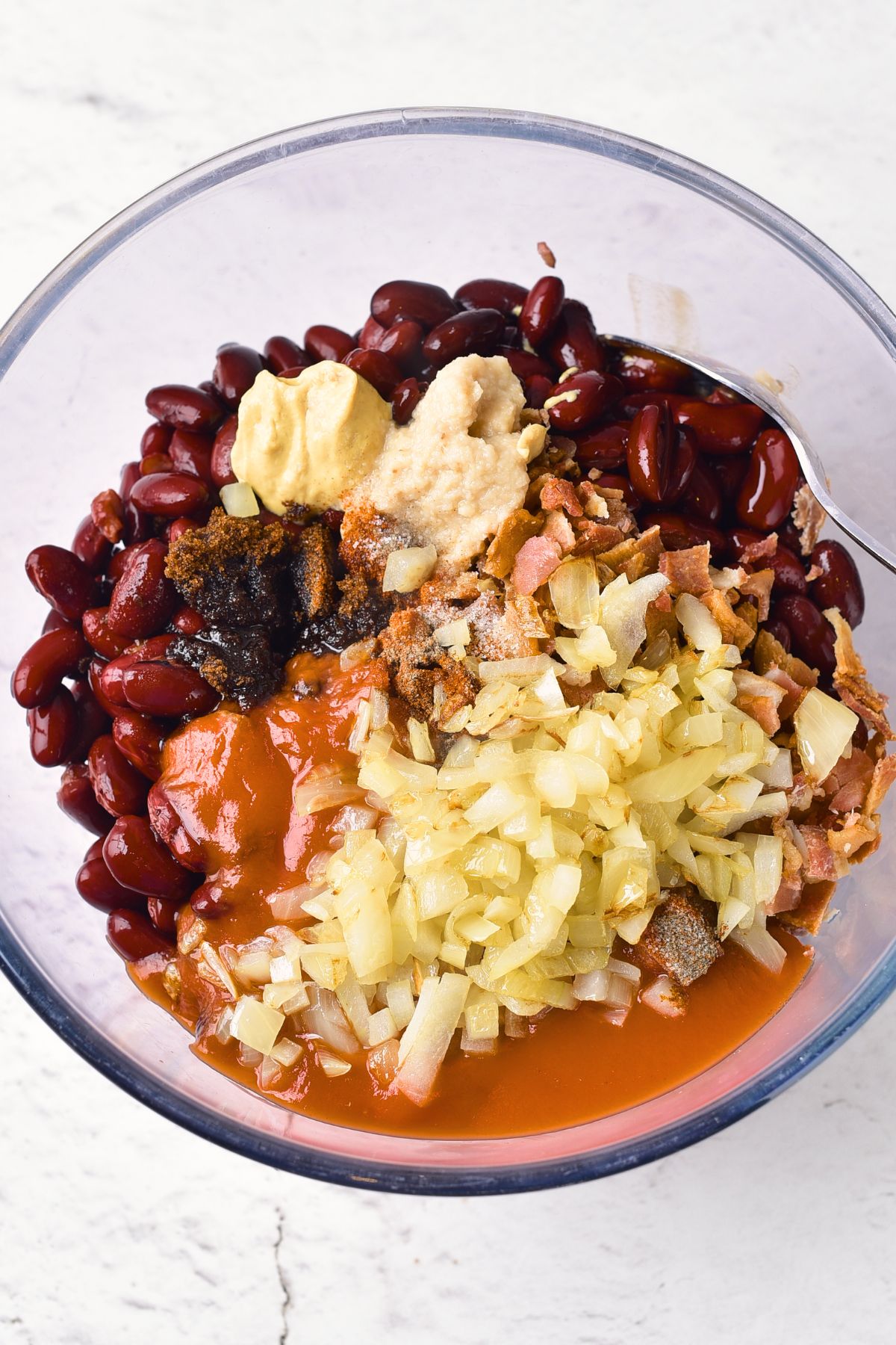 Beans, sautéed onions, fried bacon, and condiments in glass bowl.