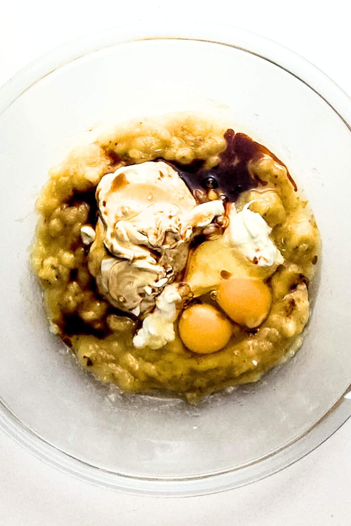 Eggs, sour cream, vanilla extract and mashed bananas in glass bowl.