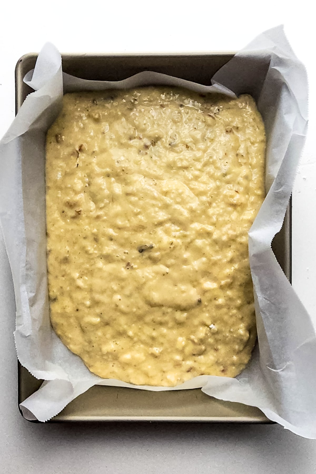 Gluten-free banana batter in parchment-lined baking pan.