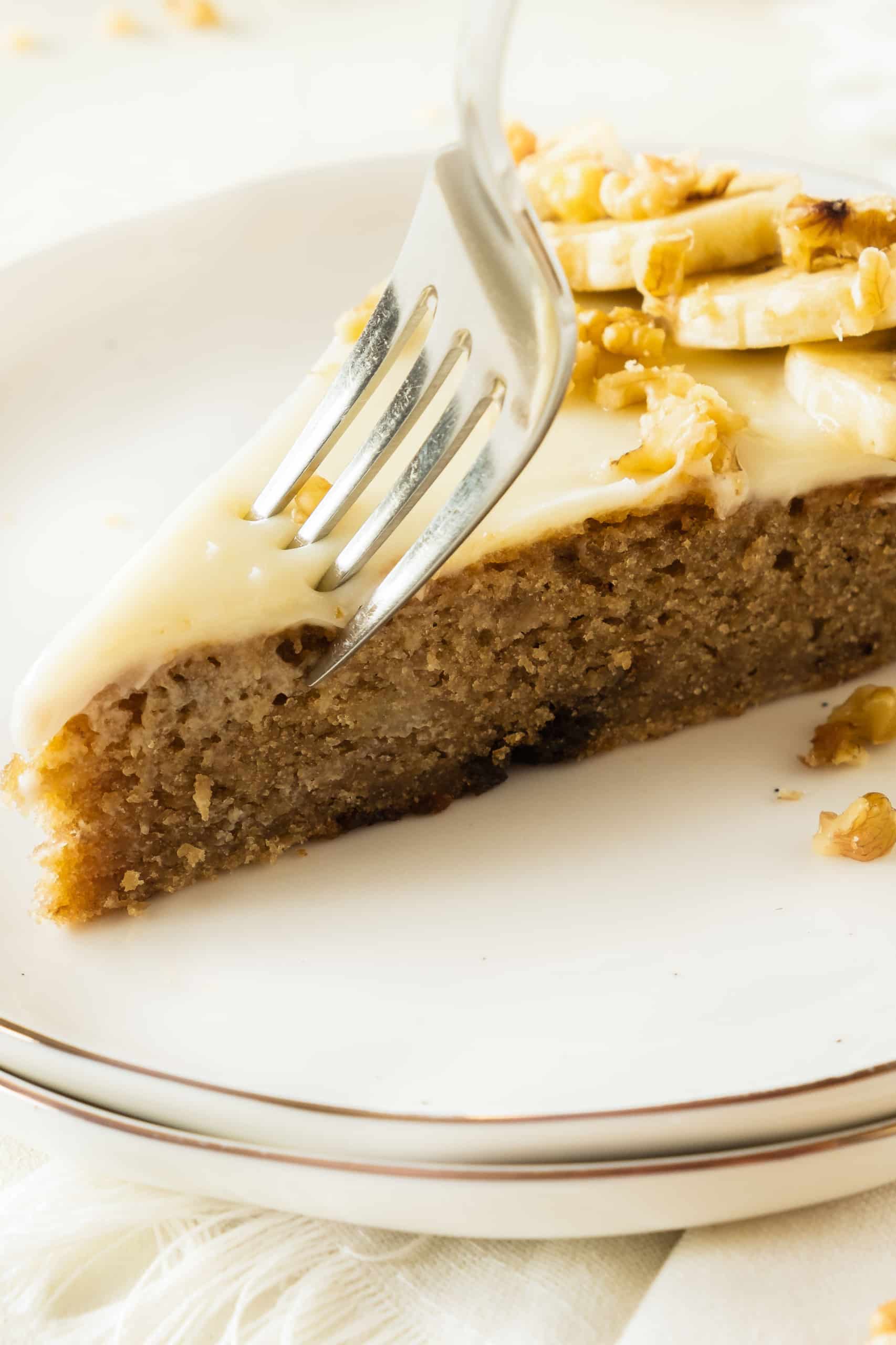 Cutting into a slice of banana cake with cream cheese frosting.