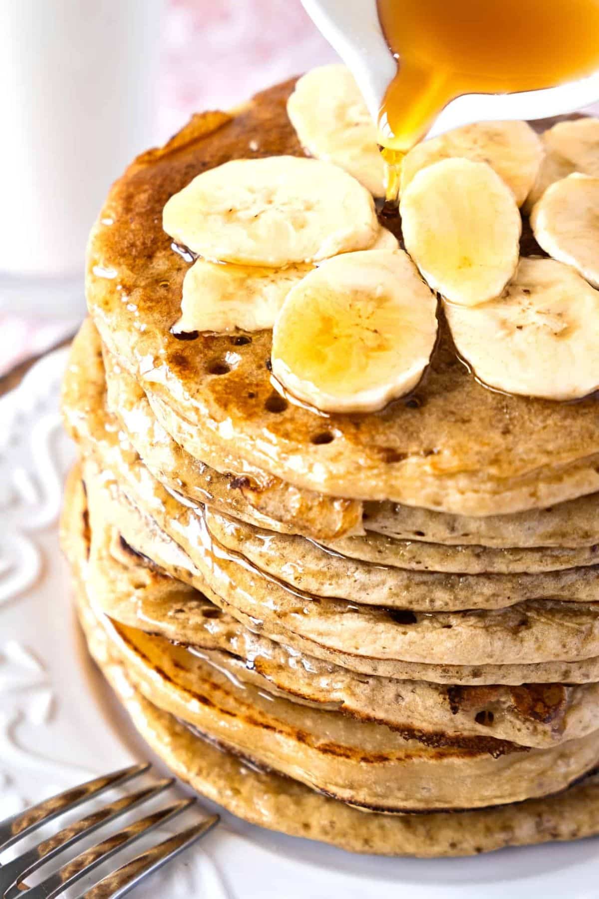 Pouring maple syrup over banana pancakes.
