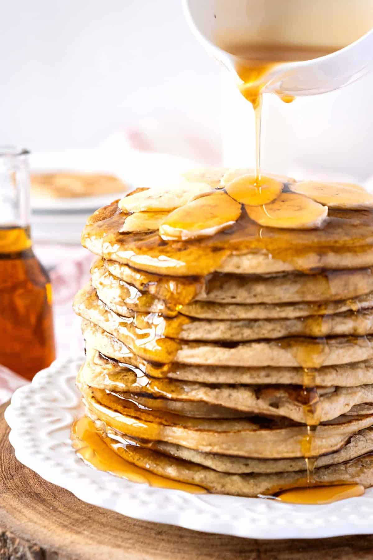 Pouring maple syrup over a stack of gluten-free dairy-free banana pancakes.