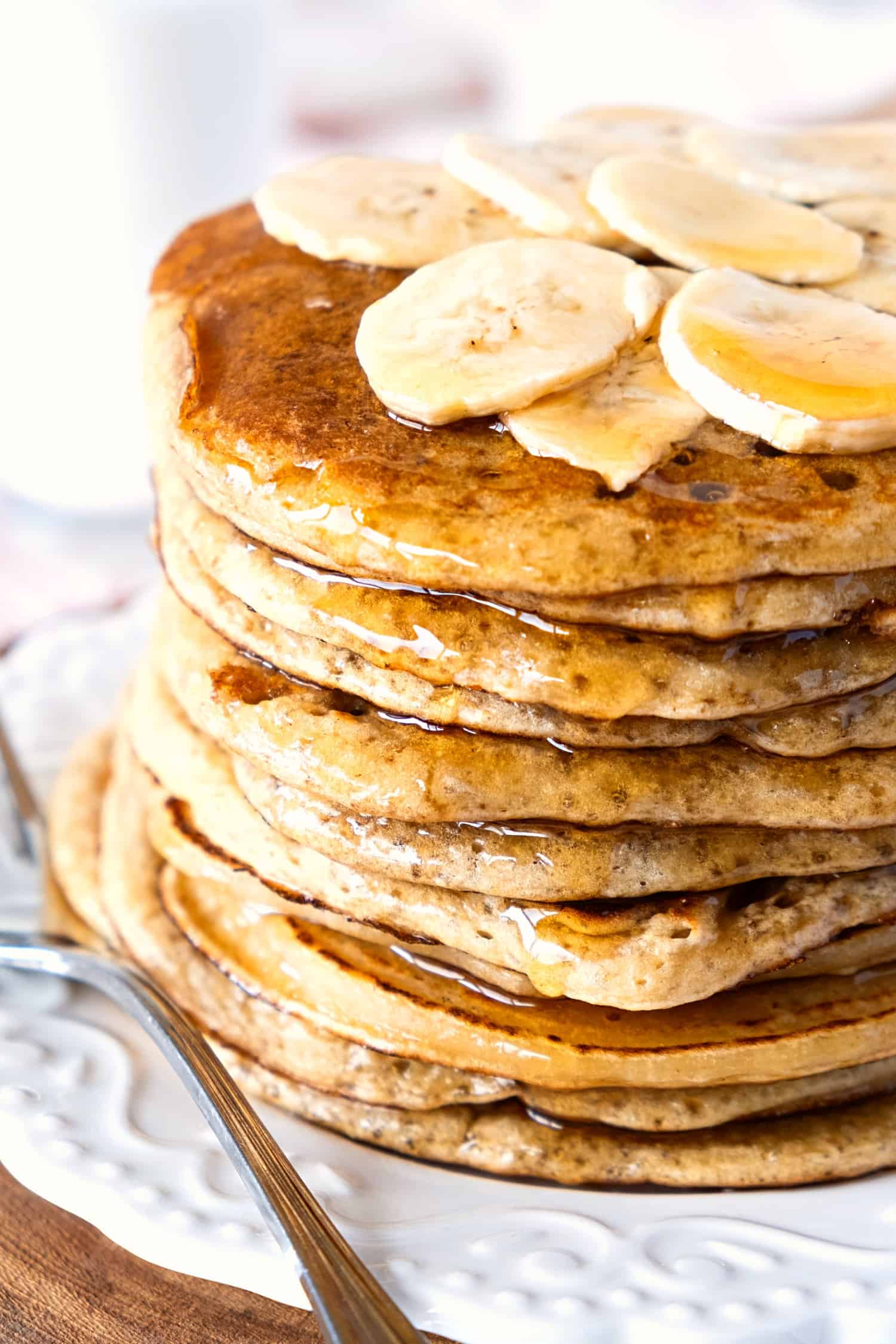 A stack of gluten-free banana pancakes topped with banana slices and maple syrup.