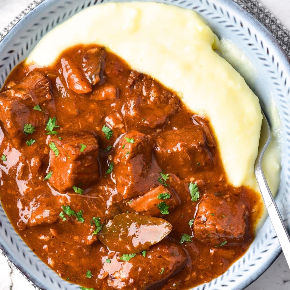 Top down view of bowl of beef bourguignon and mashed potatoes.
