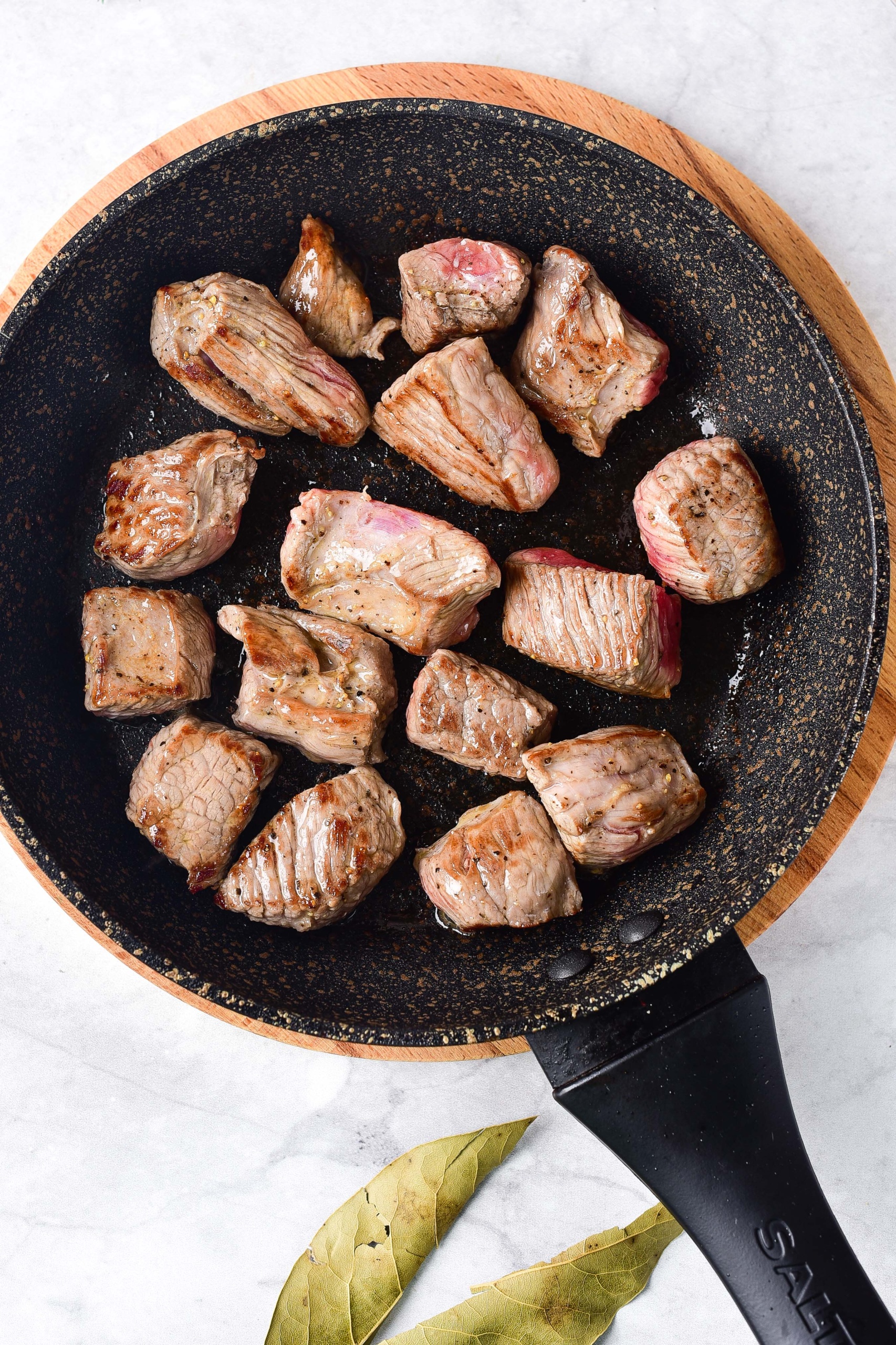 Beef cubes being seared in a skillet.