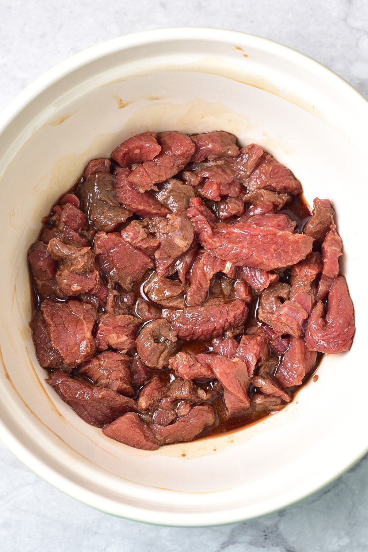 Marinating beef slices in a white bowl.