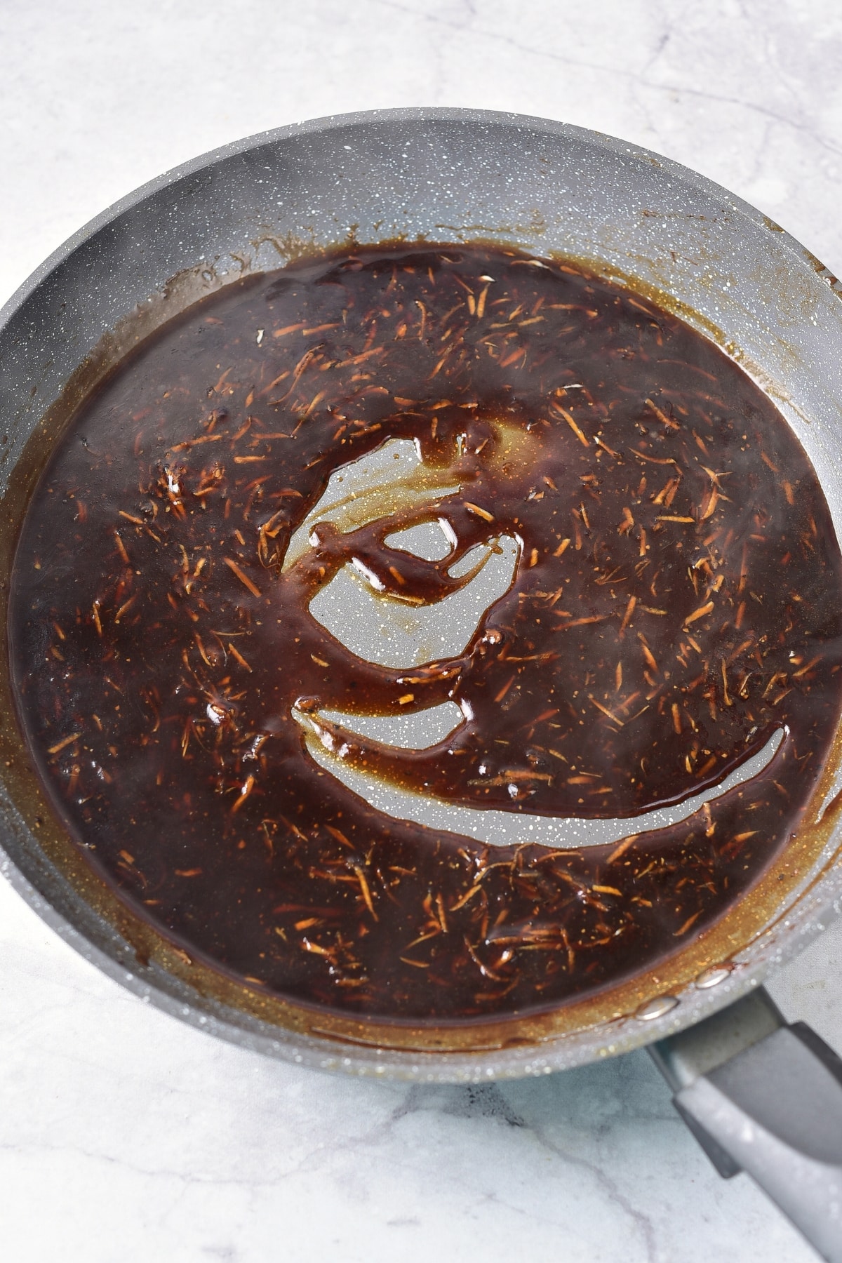 Heating up a dark brown sauce in skillet.