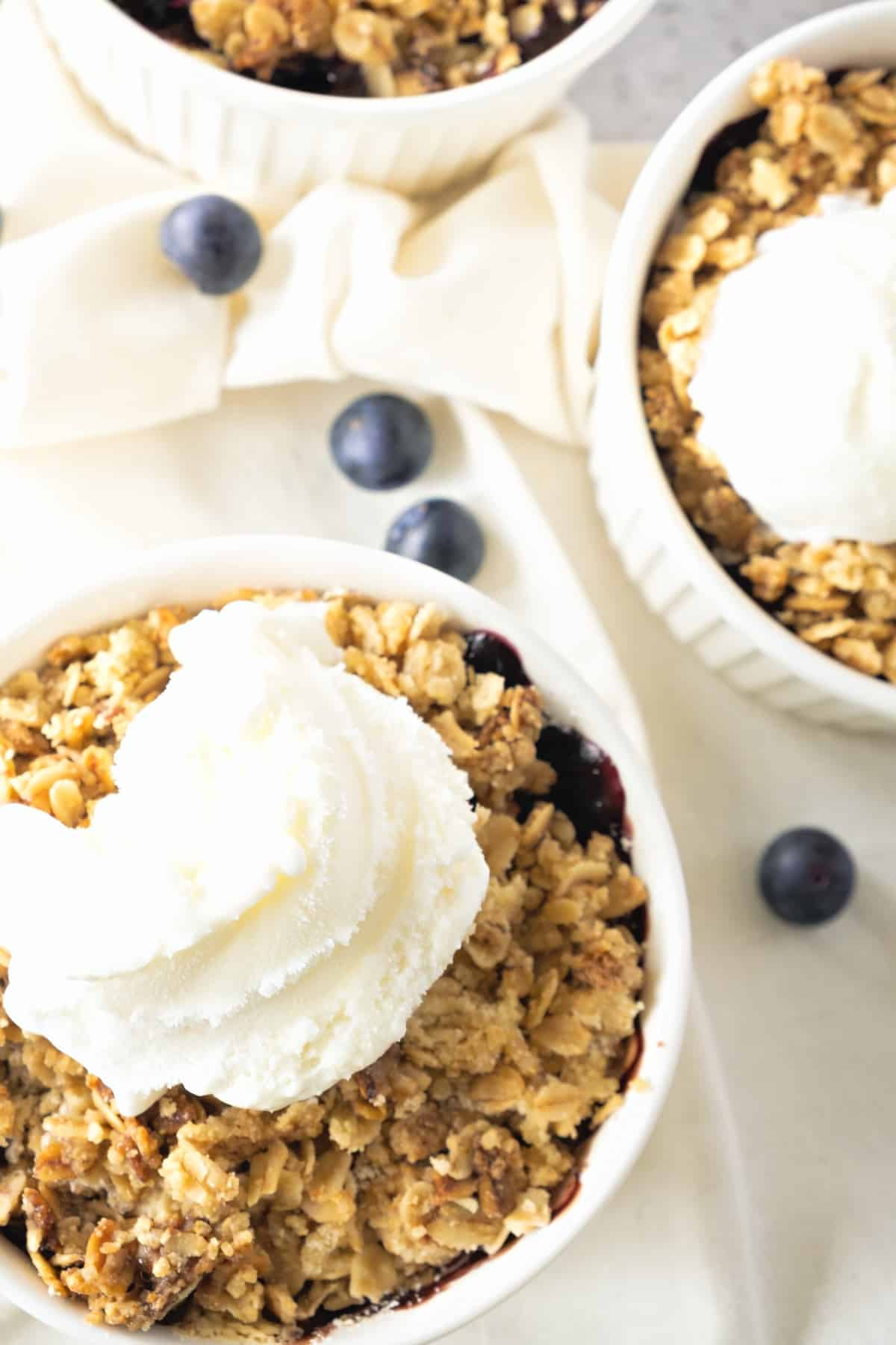 Up close shot of a ramekin with blueberry crisp and topped with ice cream.