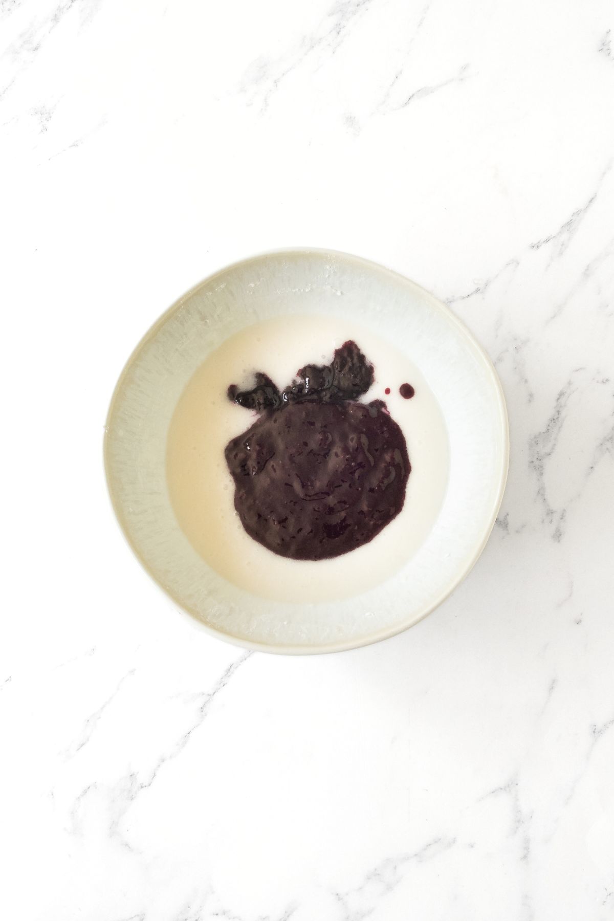 Blueberry puree in bowl of white mixture