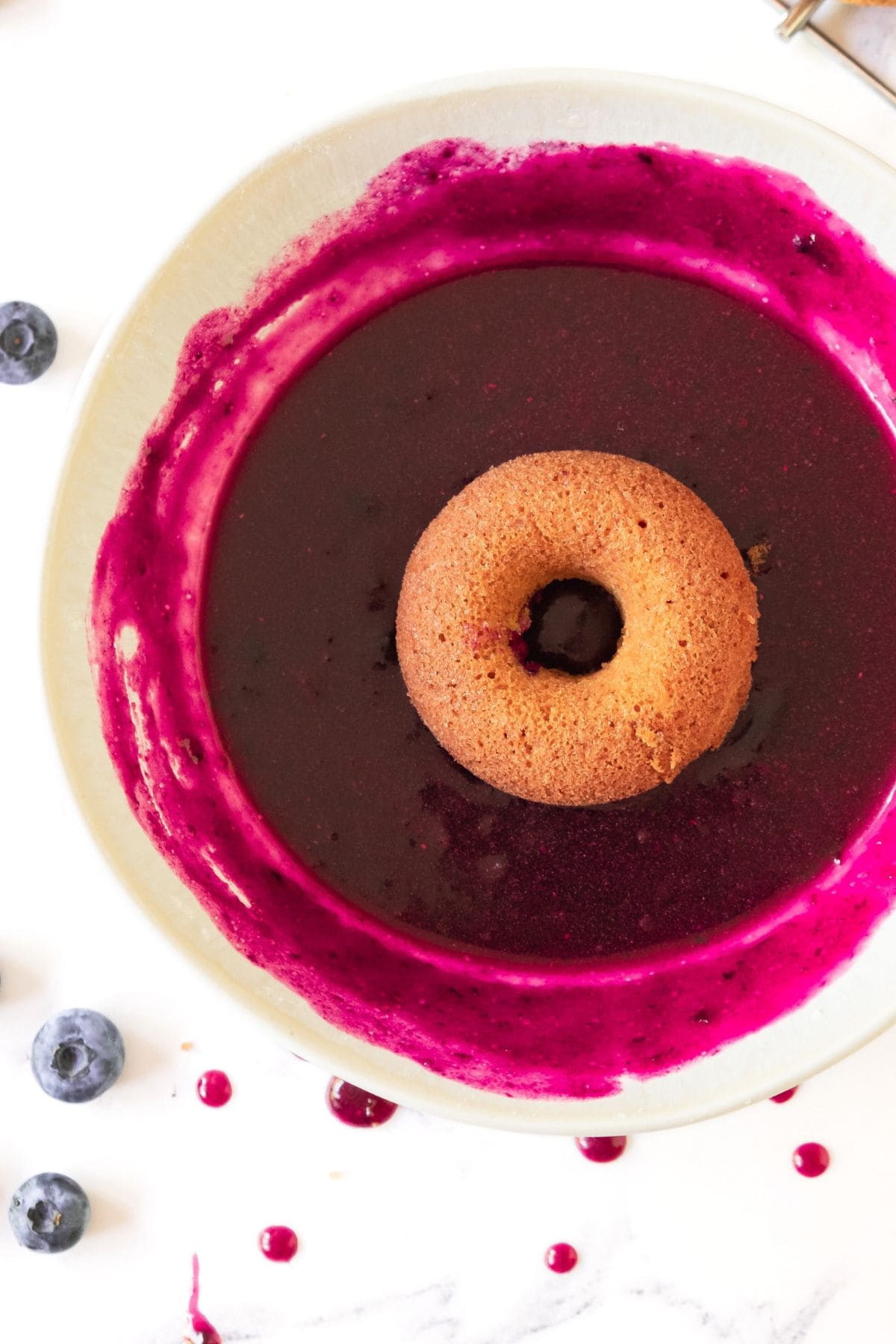 A donut in a bowl of homemade blueberry glaze