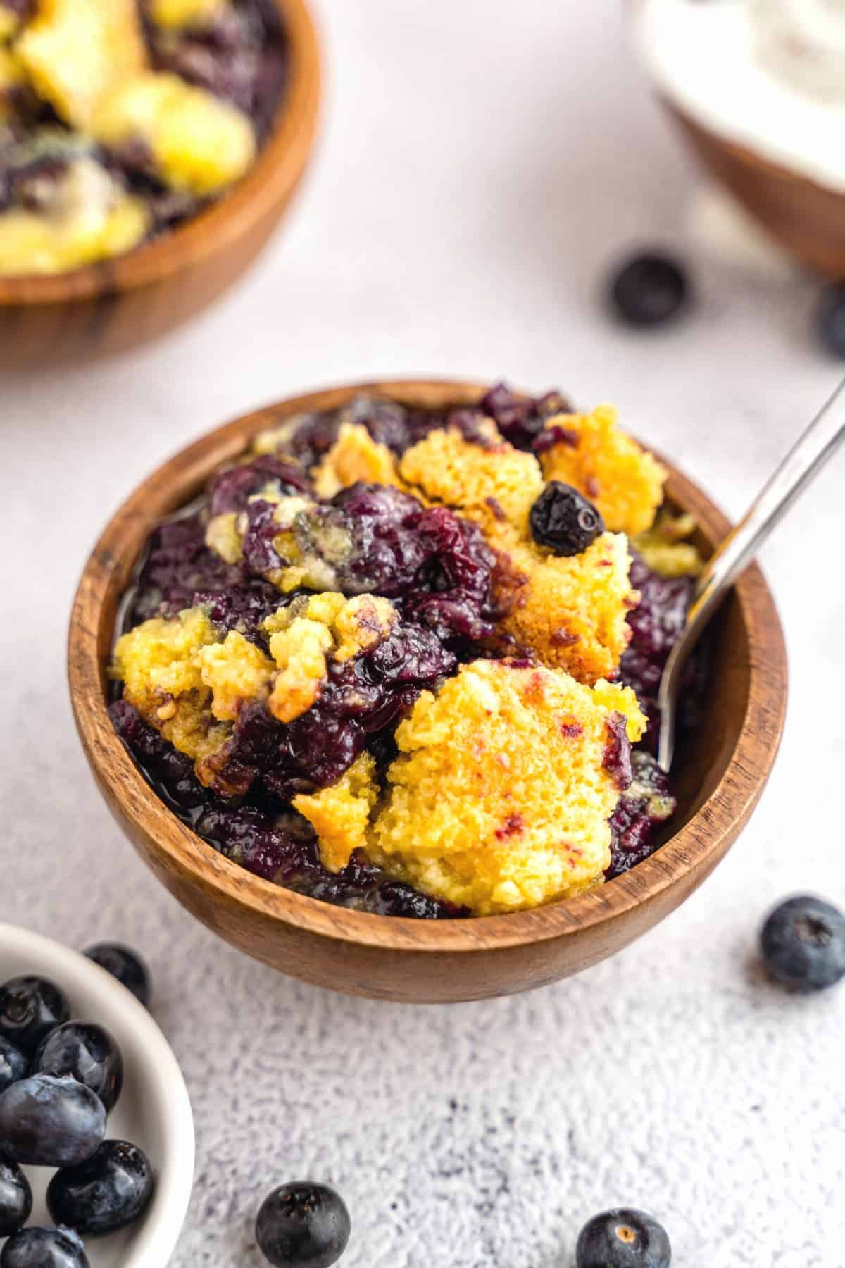A spoon in a wooden bowl with blueberry dump cake.