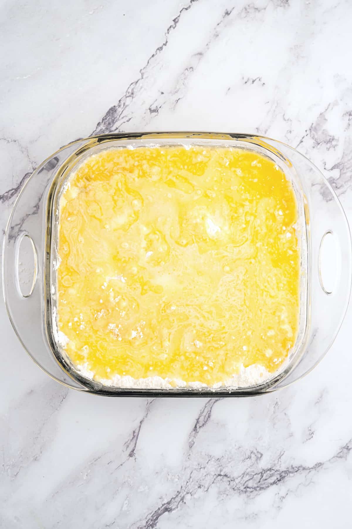Flour topped with melted butter mixture in glass pan.
