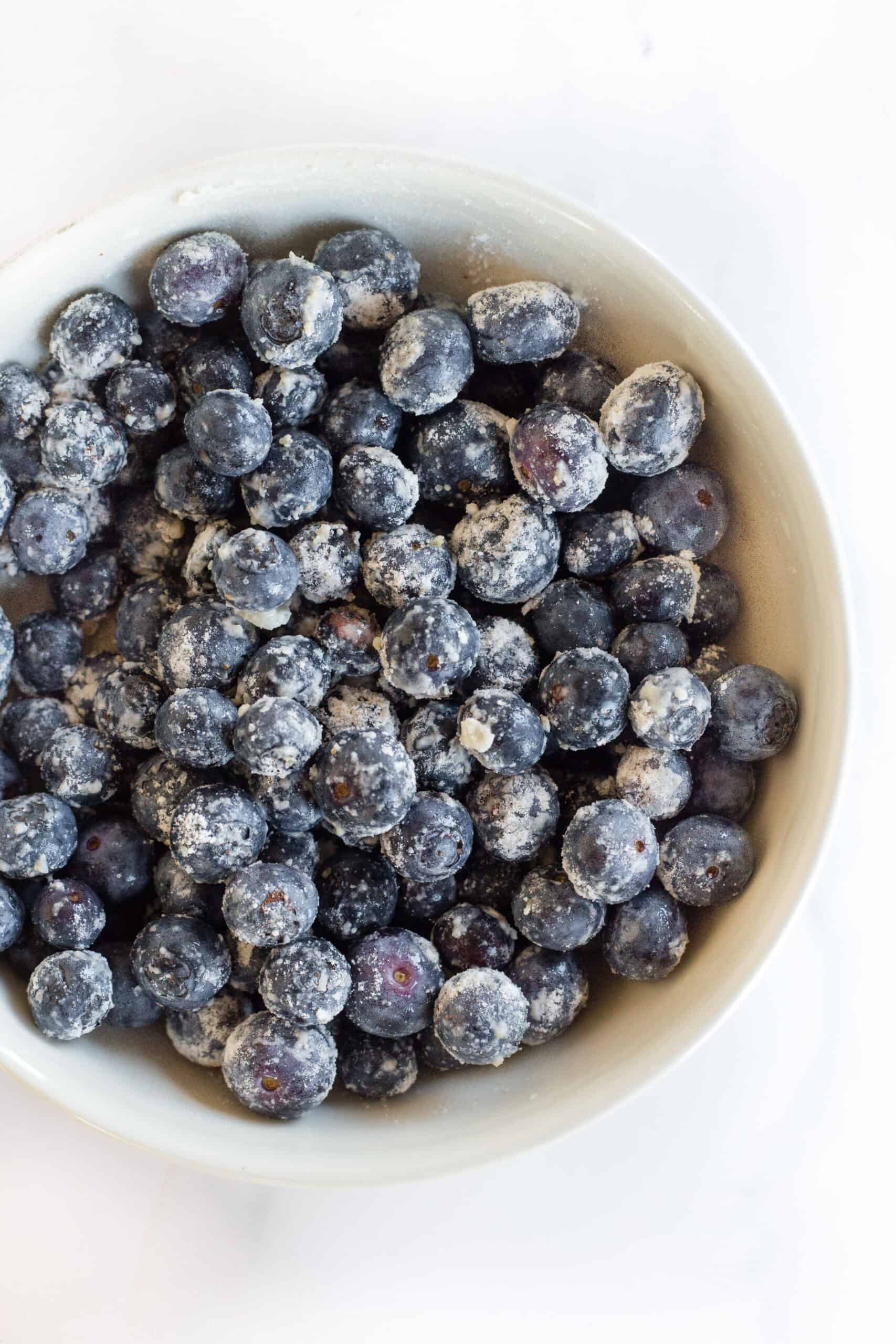 Flour-coated blueberries in a white bowl.