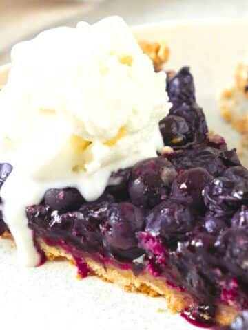 A slice of blueberry pie topped with ice cream.