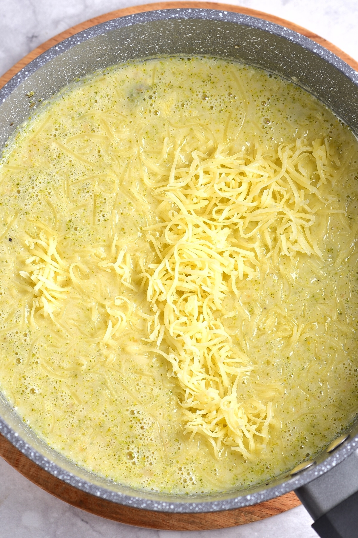 Shredded cheddar cheese in a pot of gf broccoli cheddar soup.