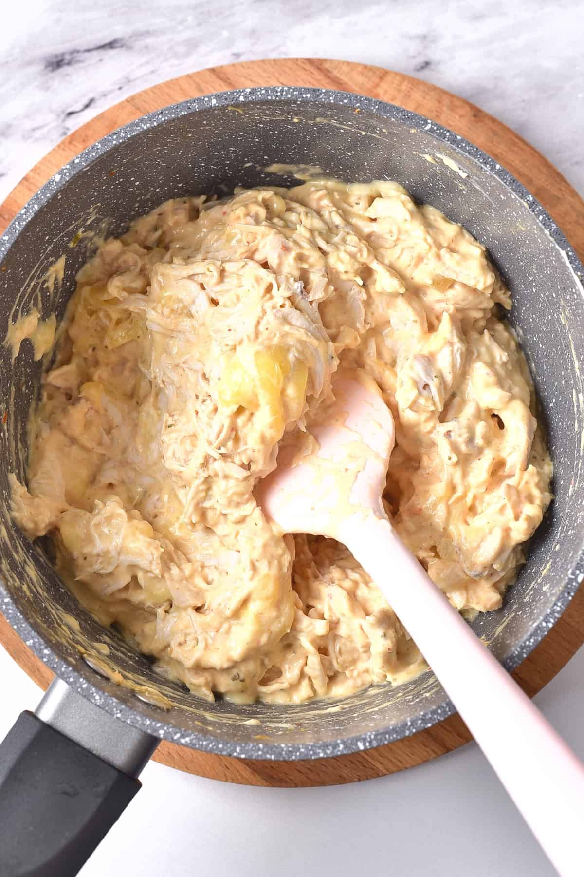 Mixing a creamy chicken mixture in a saucepan.