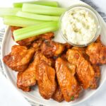 A plate of buffalo wings, celery sticks and ranch dressing.