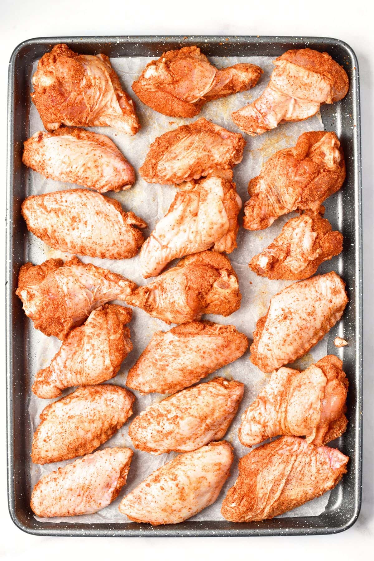 Seasoned chicken wings on parchment-lined baking sheet
