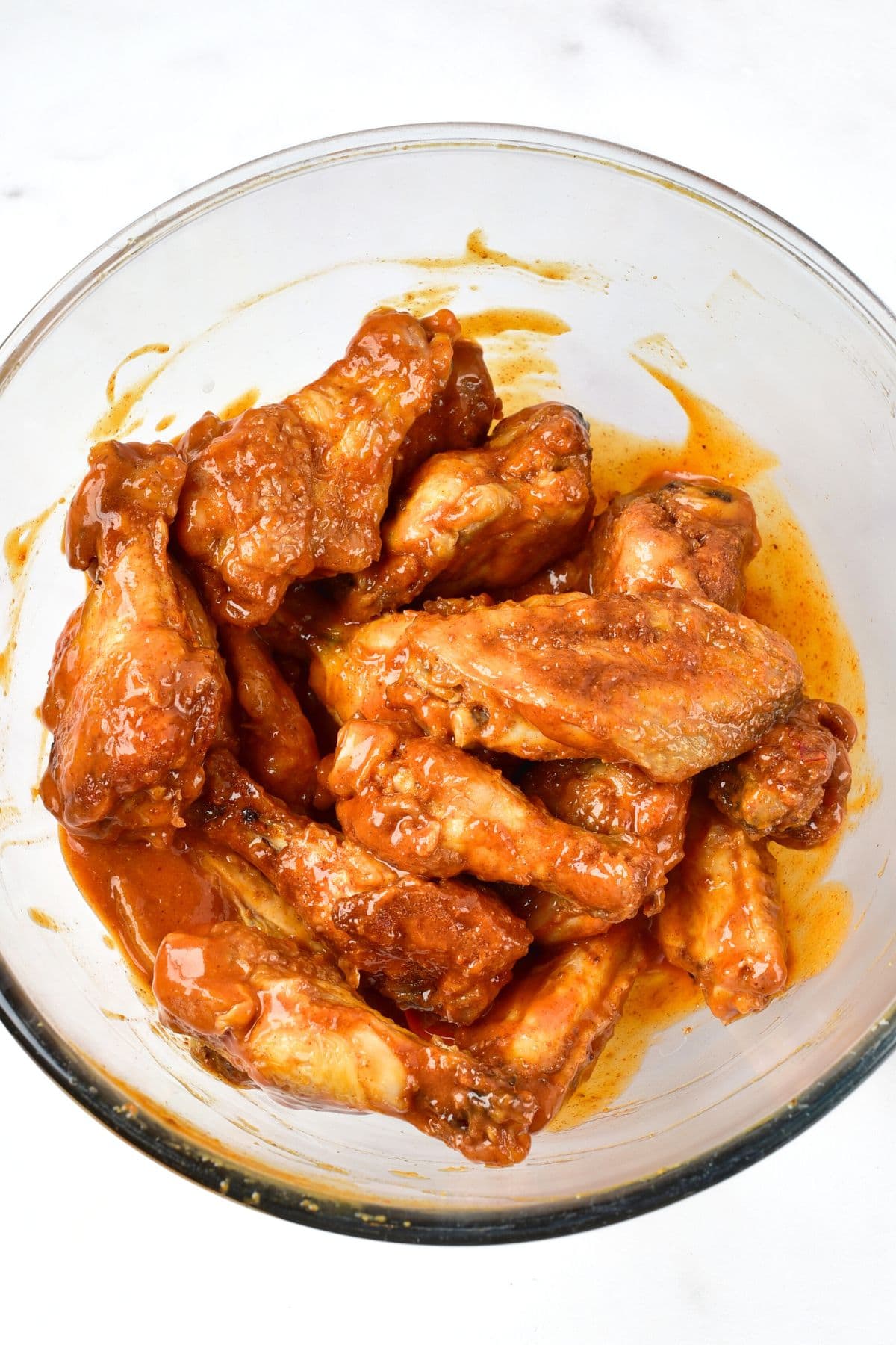 Chicken wings tossed in buffalo sauce in glass bowl.