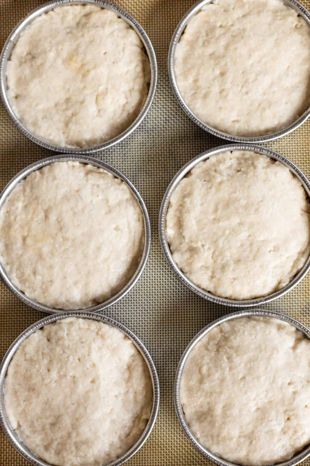 Gluten-free hamburger bun dough rising in metal rings.