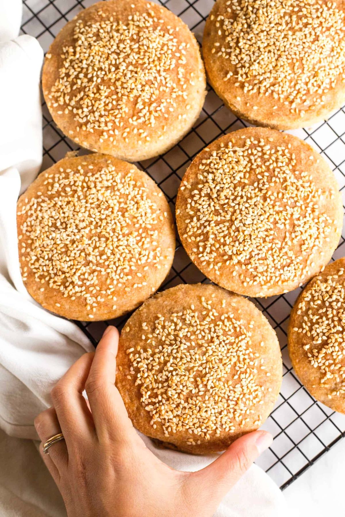 Hand reaching for a gluten-free hamburger bun from wire rack.