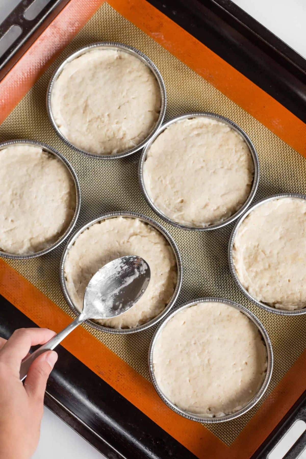 Pressing gluten-free bun dough into round metal rings.