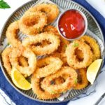 A plate of fried calamari, lemon wedges and ketchup.