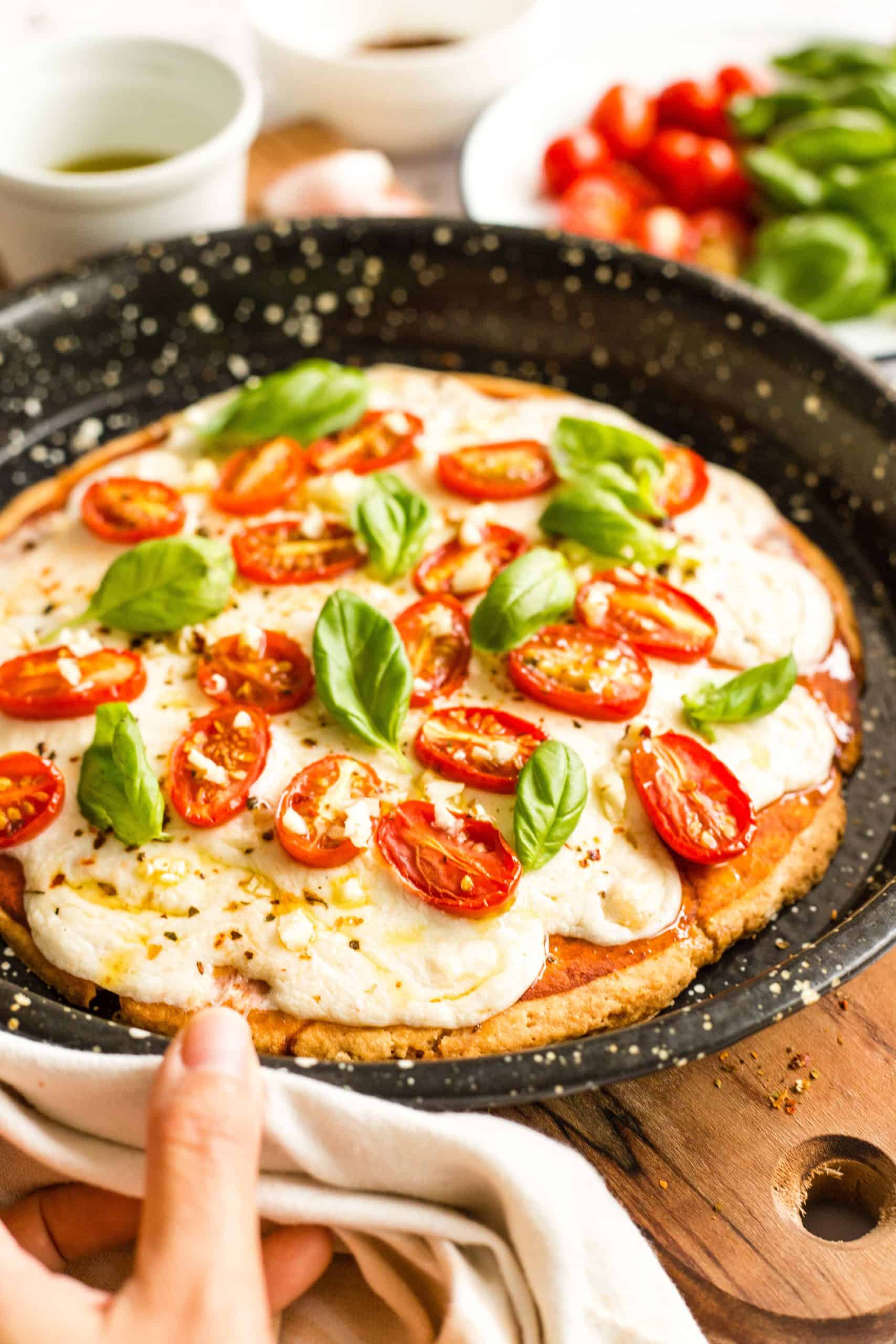 Hand holding a pizza pan with a freshly baked gluten-free caprese pizza. 