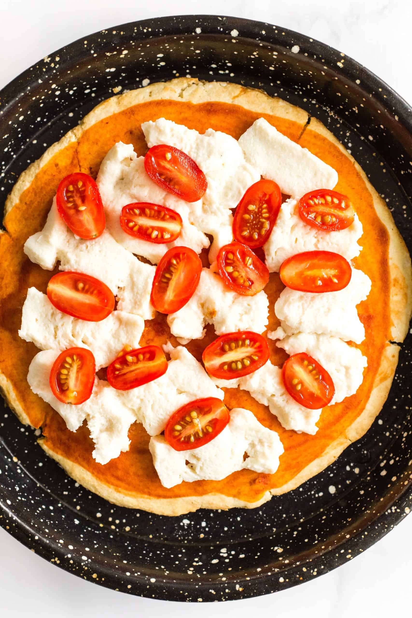 Gluten-free pizza crust with mozzarella cheese and cherry tomato halves.