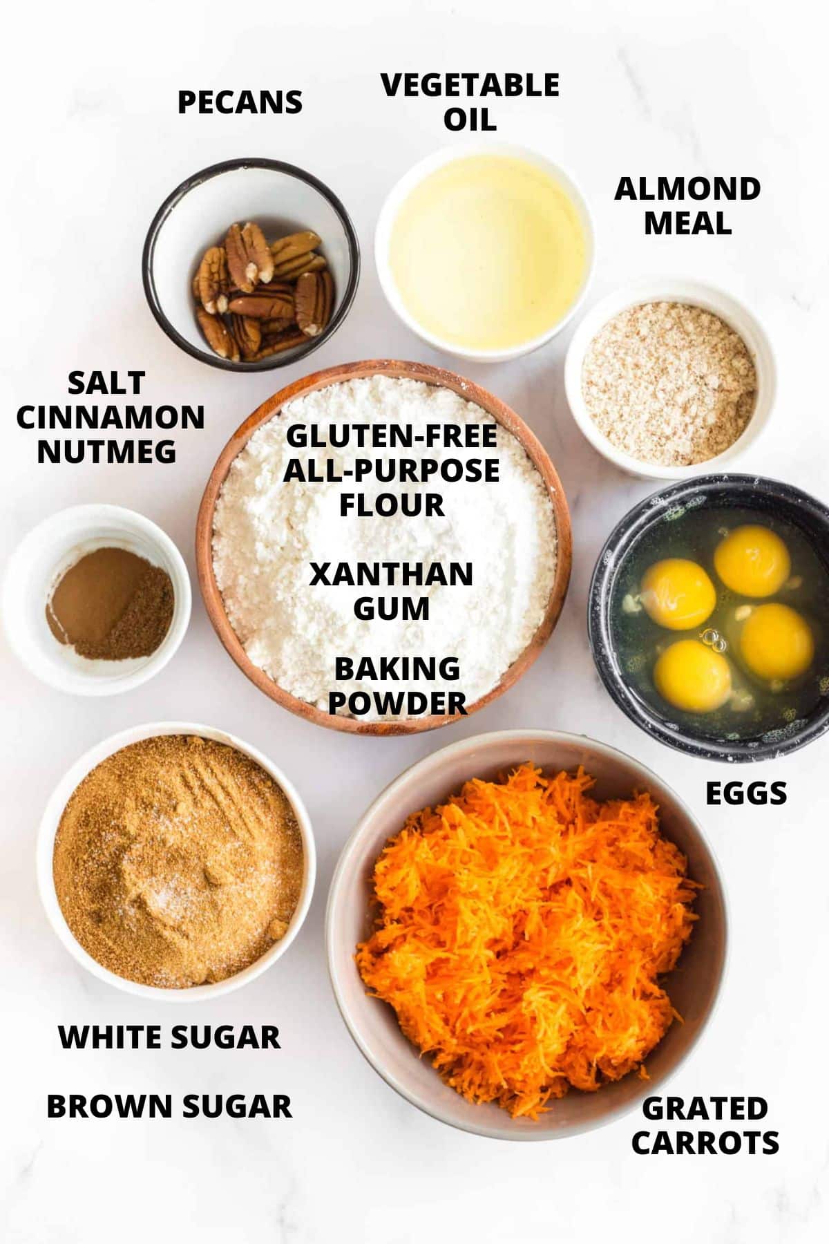 Top down view of ingredients for gluten-free carrot bread recipe on white board.