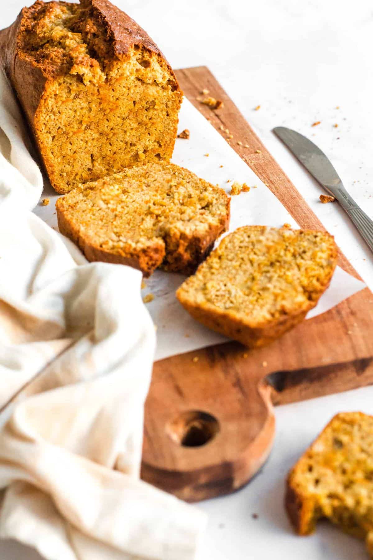 A half-sliced loaf of gluten-free carrot cake bread on parchment-lined board.
