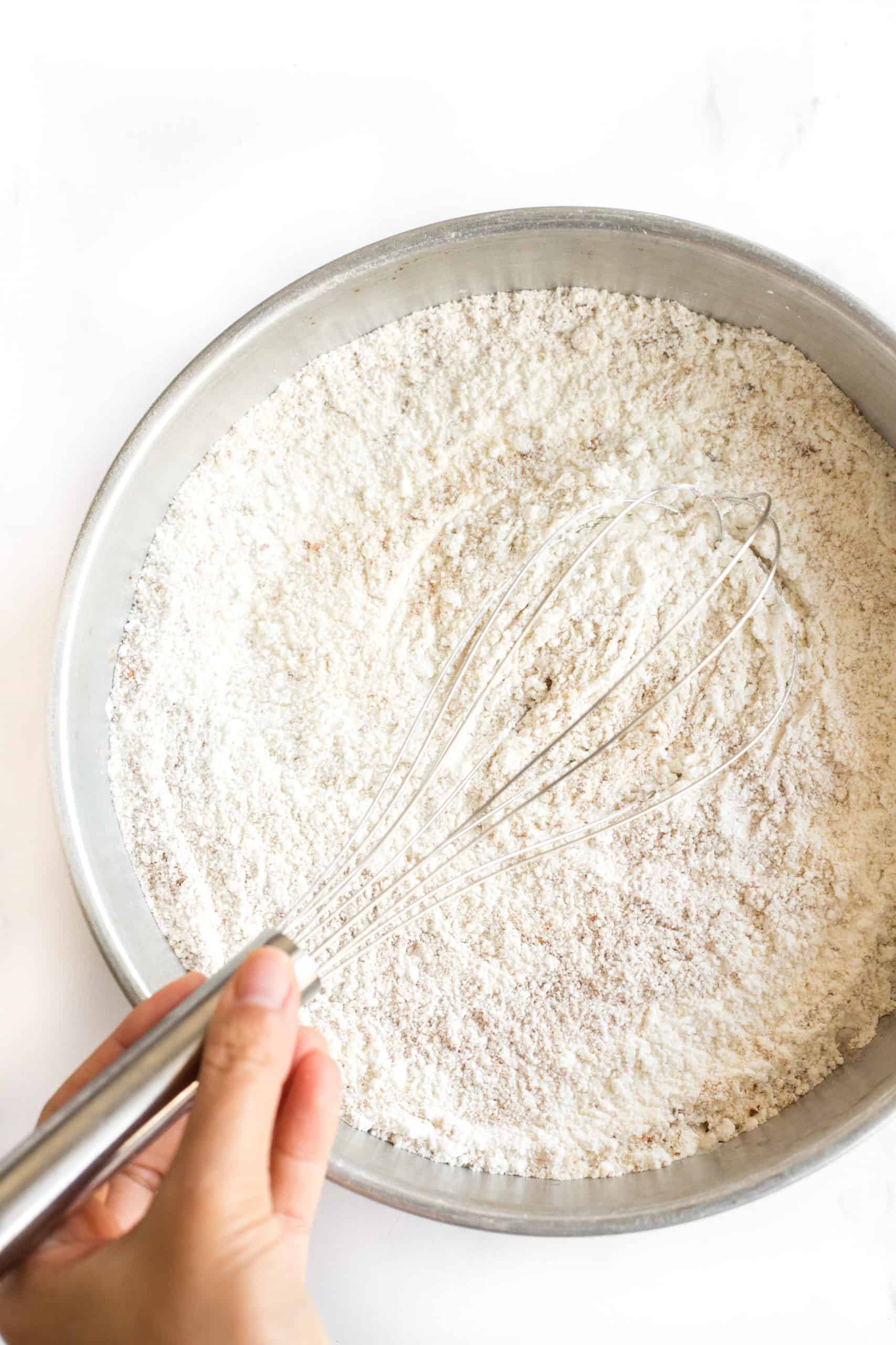 Hand whisking flour in a metal bowl.