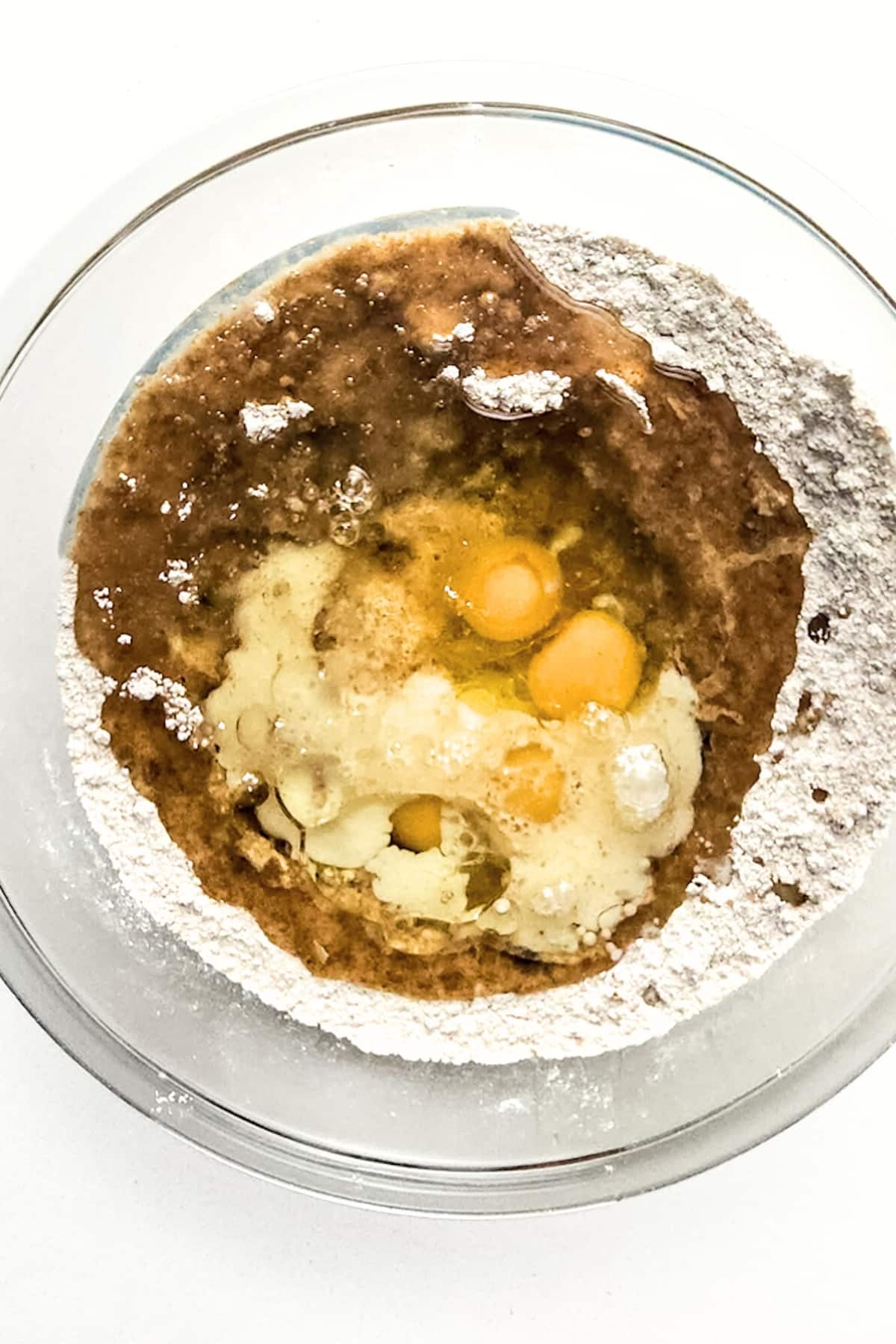 Wet ingredients on top of dry ingredients in glass bowl.