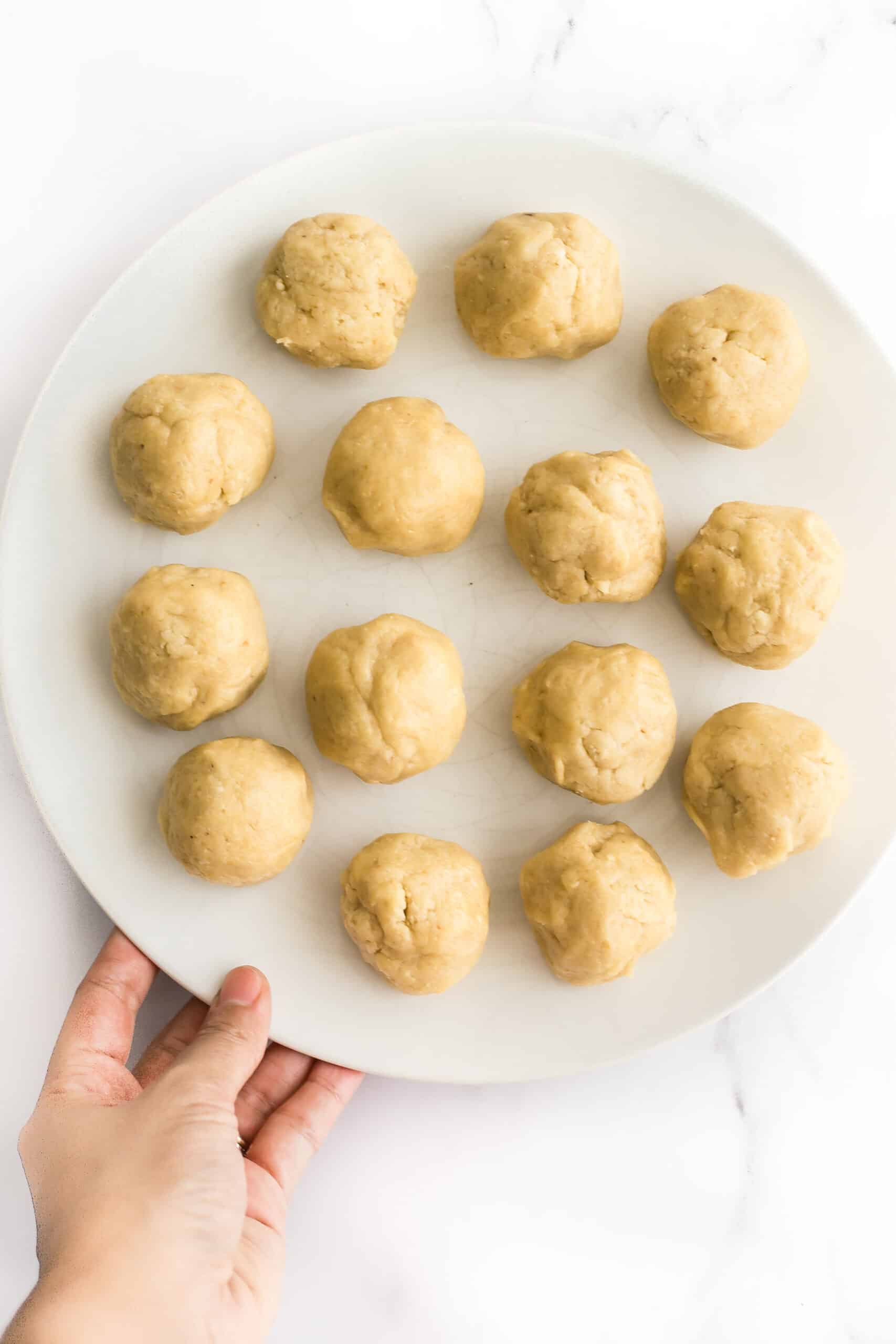 Hand holding a plate full of cashew cookie dough balls.