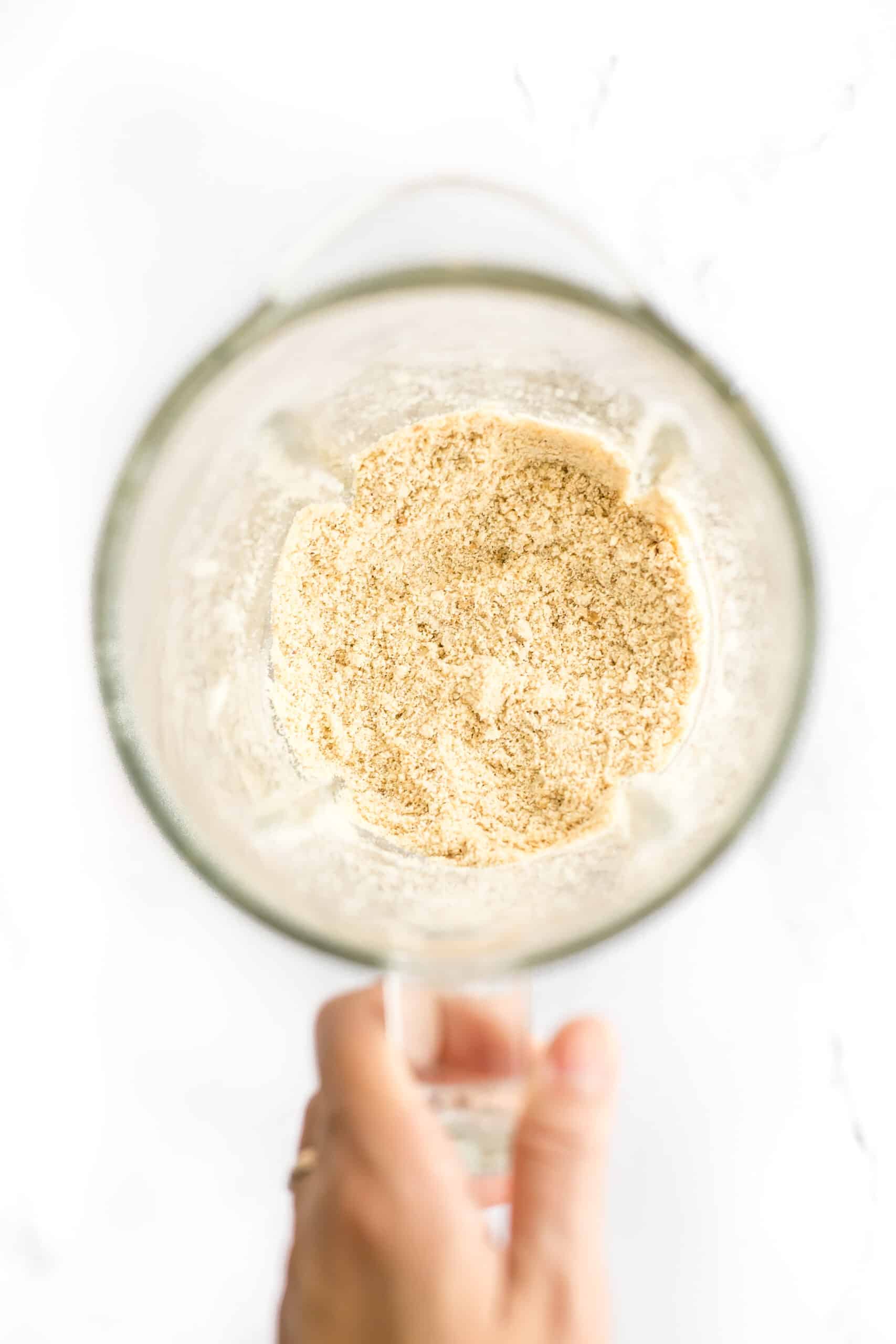 Hand holding a blender with freshly ground cashew flour.