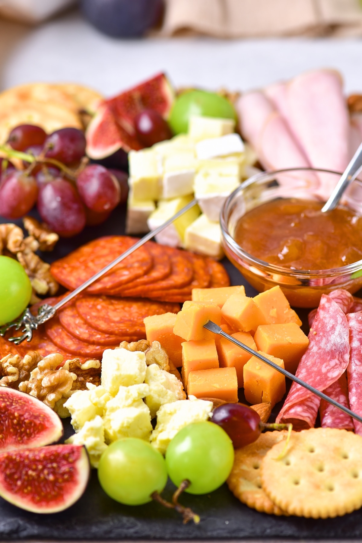 Figs, grapes, crackers and deli meats on board.