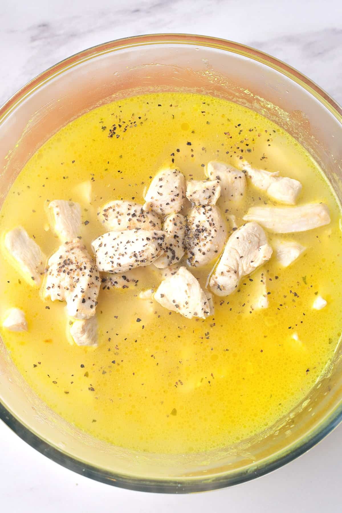 Cooked chicken pieces in a yellow liquid mixture in a glass bowl.