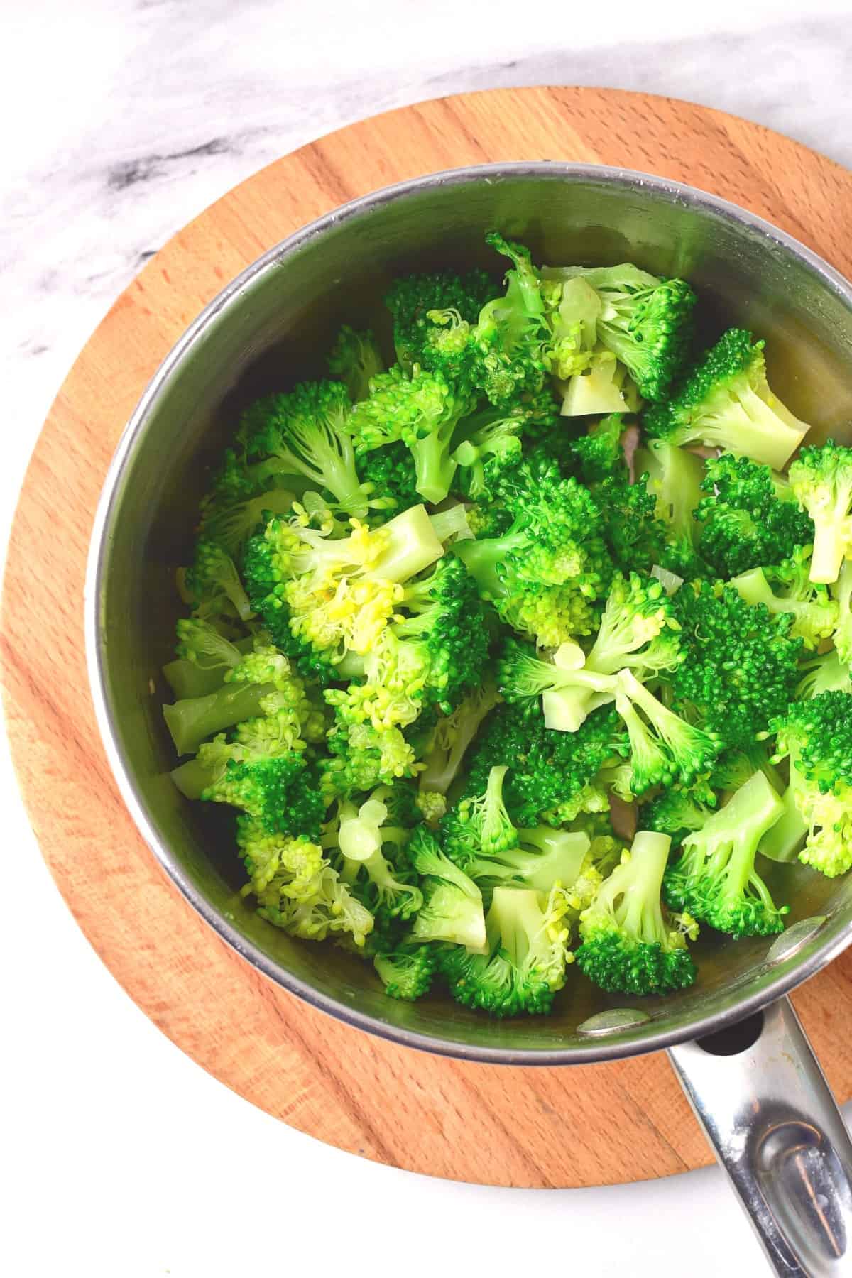 Blanched broccoli florets in a metal pot.