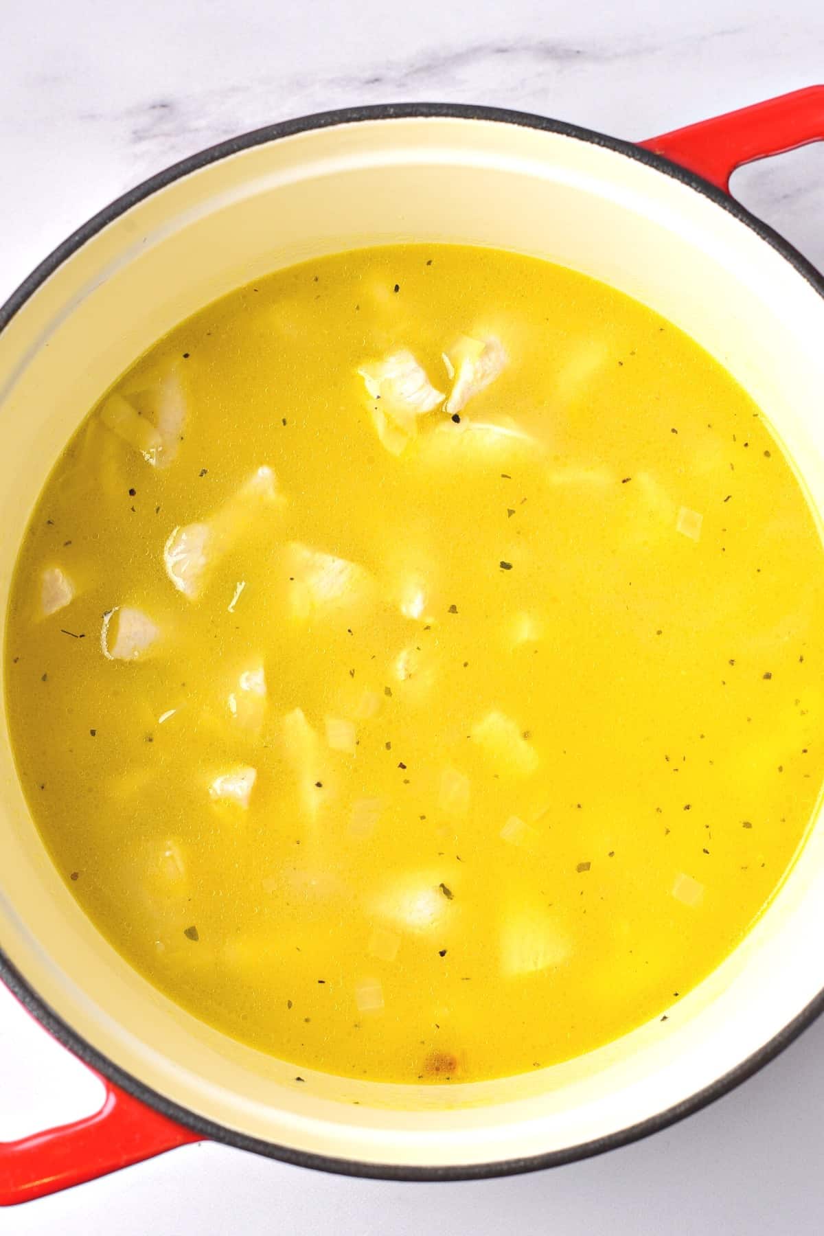 Yellow mixture with chicken pieces in Dutch oven.
