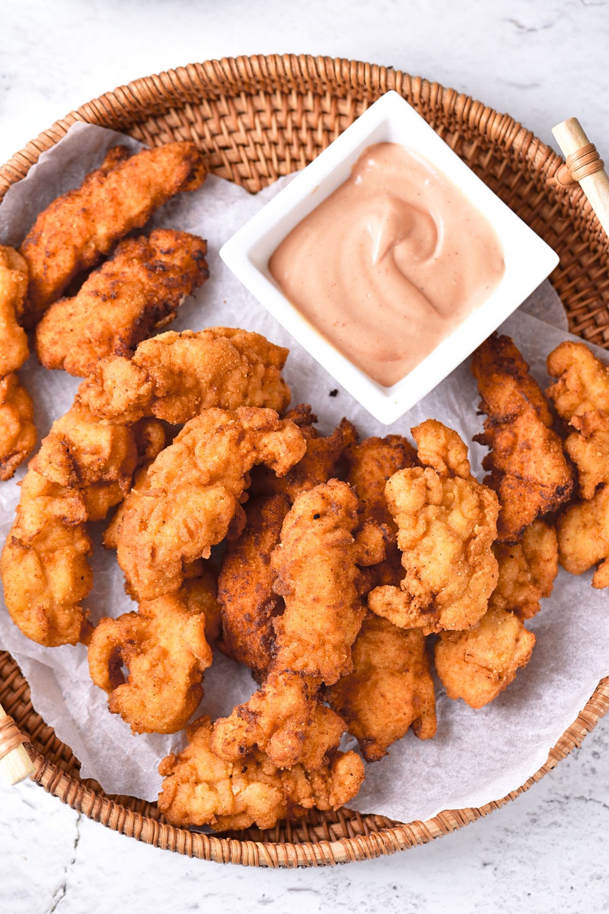 Top down view of a basket of gluten-free chicken fingers and a bowl of sauce.