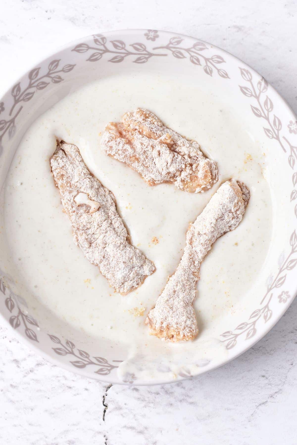 Dipping flour-coated chicken strips in buttermilk.
