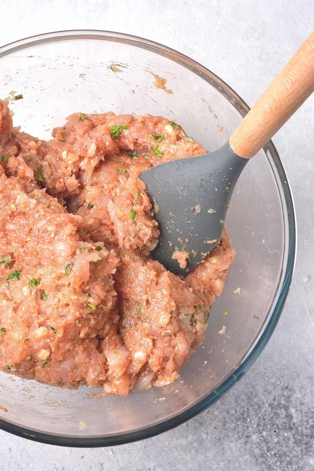 Using a spatula to mix chicken meatball mixture.