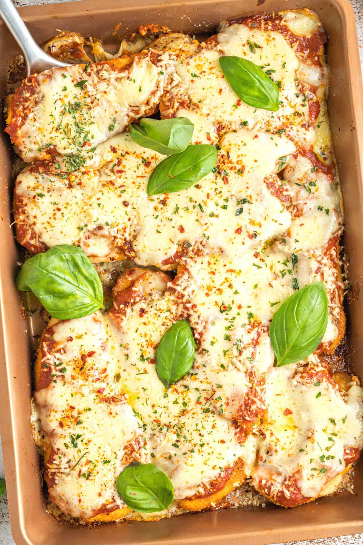 Chicken parmesan garnished with fresh basil leaves and red chili pepper flakes.