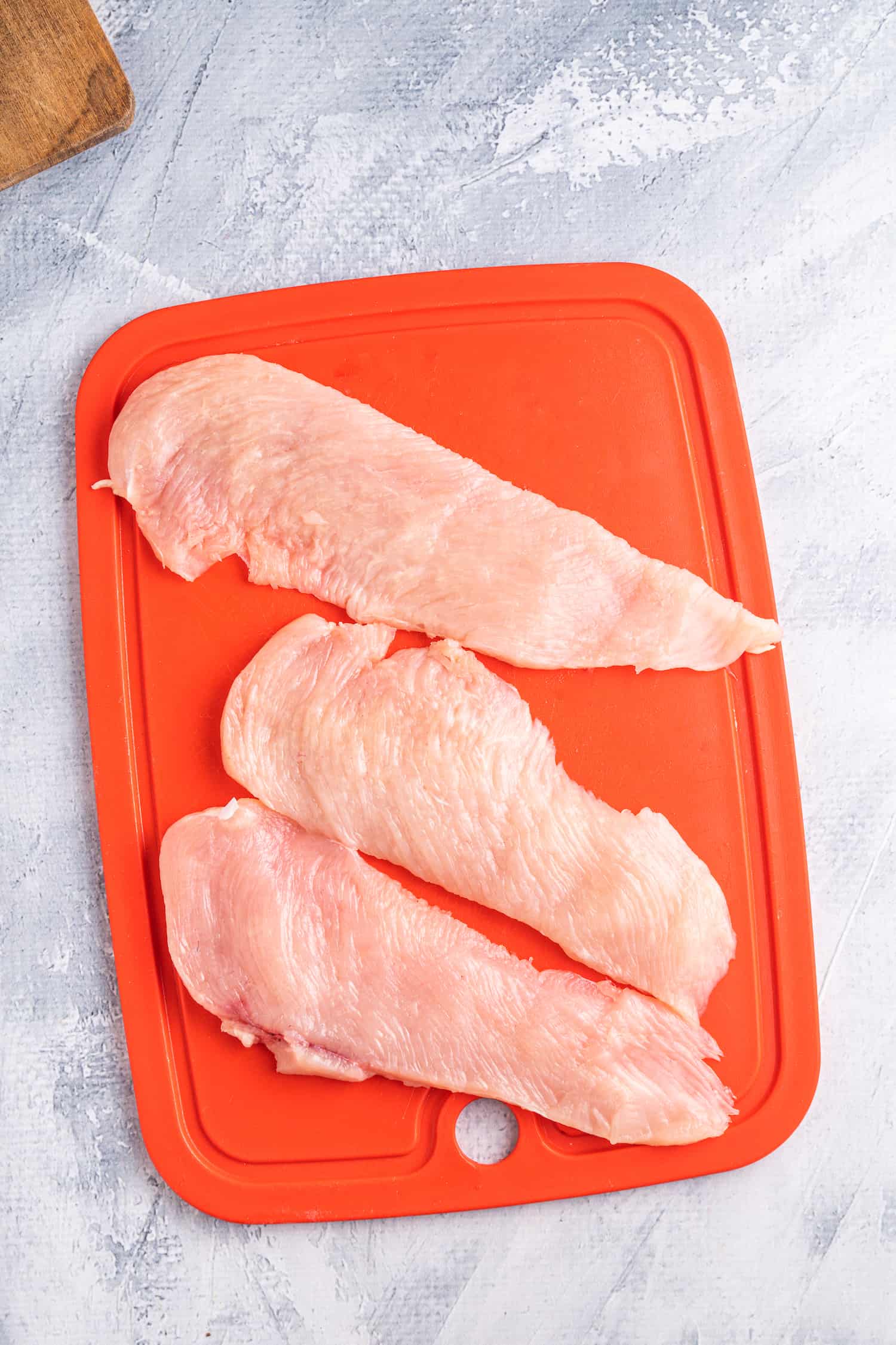 Thinly sliced chicken fillets on a red chopping board.