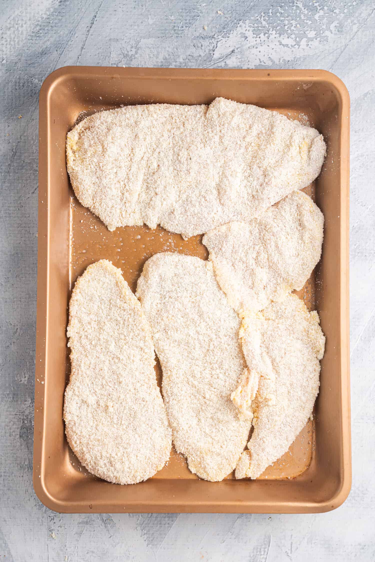 Breaded chicken fillets on a baking tray ready to be baked.
