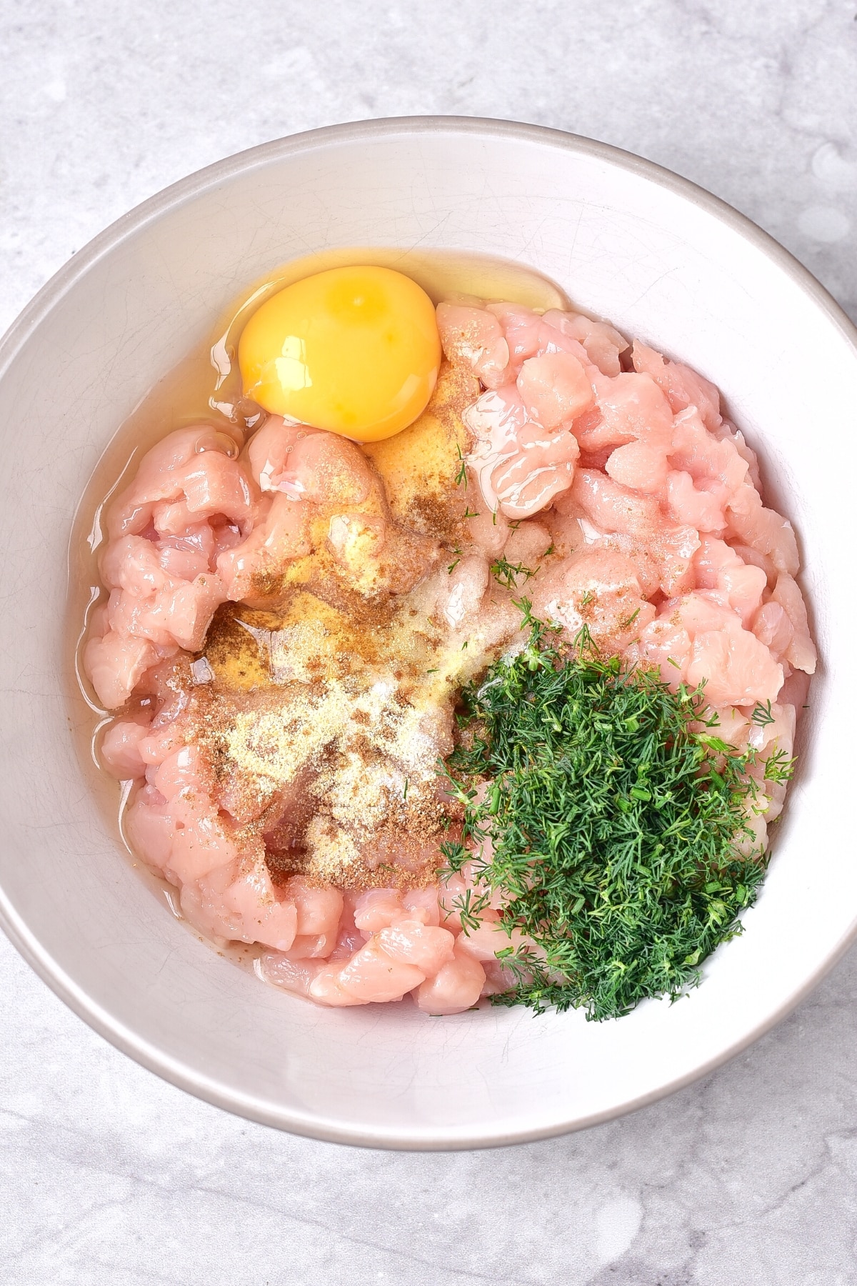 Chopped chicken, fresh dill and condiments in a white bowl.