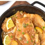 Top down view of a skillet with chicken in sauce topped with lemon.