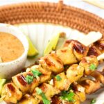 A plate of satay chicken skewers on bamboo tray.